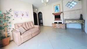 A living room with a sofa, a dining table, a chandelier, and a fireplace. - Casa com Piscina em Cabeçudas , 80 metros da Praia (Itajaí)