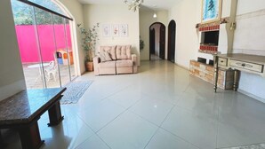 A spacious living area with a sofa, a dining table, a chandelier, and a fireplace. - Casa com Piscina em Cabeçudas , 80 metros da Praia (Itajaí)