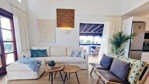 Un salon avec un canapé, une table basse et un fauteuil. On y trouve une plante, une œuvre d’art murale et une fenêtre.