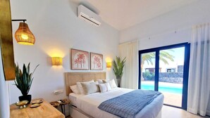 Une chambre avec un lit, une table de chevet, une lampe, un appareil de climatisation et une vue sur une piscine.