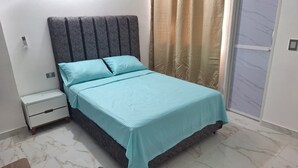 A bed with a grey headboard, a white nightstand, and a window with curtains. - Comfortable room with separate entrance (Barrancabermeja)