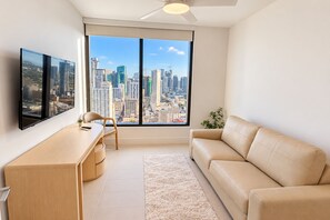 Un salon moderne doté d’une grande fenêtre, d’un bureau, d’une chaise, d’un canapé et d’un ventilateur de plafond.