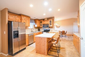 A modern kitchen with wooden cabinets, stainless steel appliances, and a central island with bar stools. - Haven in the Canyons: Hot Tub, Fire Pit, Deck Views, Boat Parking (Page)
