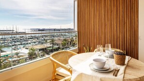 Un balcon donnant sur un port de plaisance, une table ronde dressée avec des assiettes, un bol et un verre, et un mur en bois à lattes.