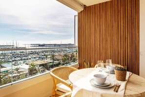 Ein Balkon mit Blick auf eine Marina, ein runder Tisch gedeckt mit Tellern, einer Schüssel und einem Glas, sowie eine Wand aus Holzlamellen.