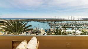 Un balcon offrant une vue sur une marina où s’alignent des bateaux, des palmiers et où le ciel est dégagé.