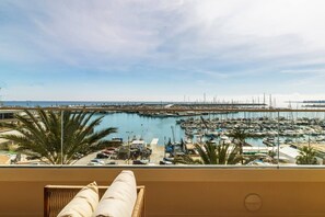 Ein Balkon mit Blick auf eine Marina voller Boote, Palmen und einem wolkenlosen Himmel.
