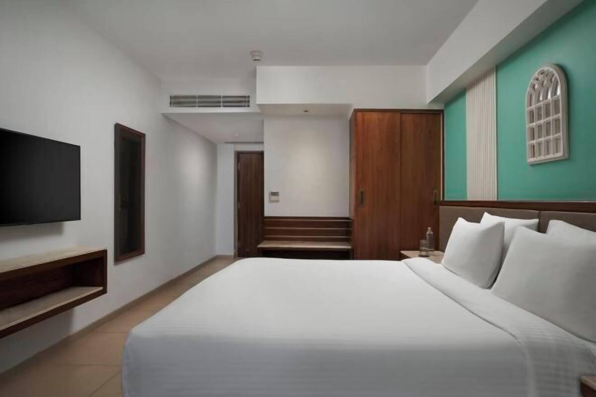 A hotel room with a bed, a TV, a wooden wardrobe, and a staircase leading to another room.