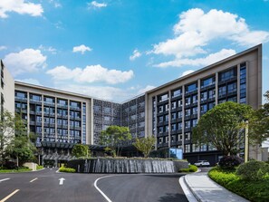 A modern building with a curved driveway, a waterfall feature, and a clear sky. - Garden Resort Kunming Changshui Airport (Kunming)