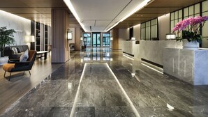 Eine moderne Lobby mit Marmorboden, einer Rezeption, einer Sitzecke und großen Fenstern.