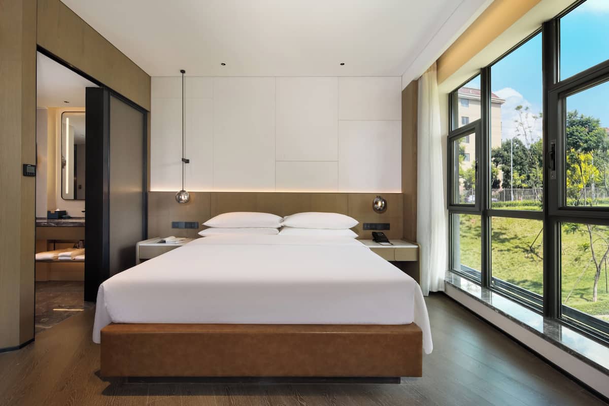 Et moderne hotelværelse med en stor seng, sengeborde, et spejl og udsigt til det fri.