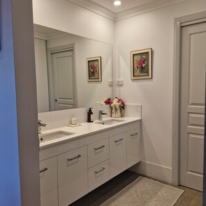 A bathroom with a double sink vanity, a large mirror, and a framed floral artwork on the wall.