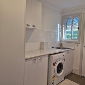 A compact laundry room with a washing machine, a sink, and a window.