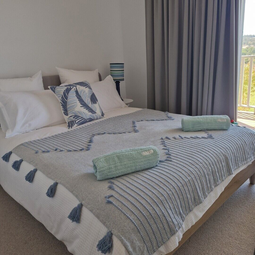 A neatly made bed with a patterned blanket, pillows, and two rolled towels.
