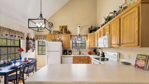 A kitchen with wooden cabinets, a dining table with chairs, a refrigerator, a coffee maker, and a magazine on the counter. - Smoky Ridge Retreat | Hot Tub • Firepit • Views (Gatlinburg)