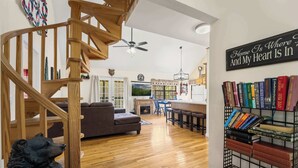 A spacious living area with a wooden staircase, a fireplace, a dining area, and a bookshelf. - Smoky Ridge Retreat | Hot Tub • Firepit • Views (Gatlinburg)