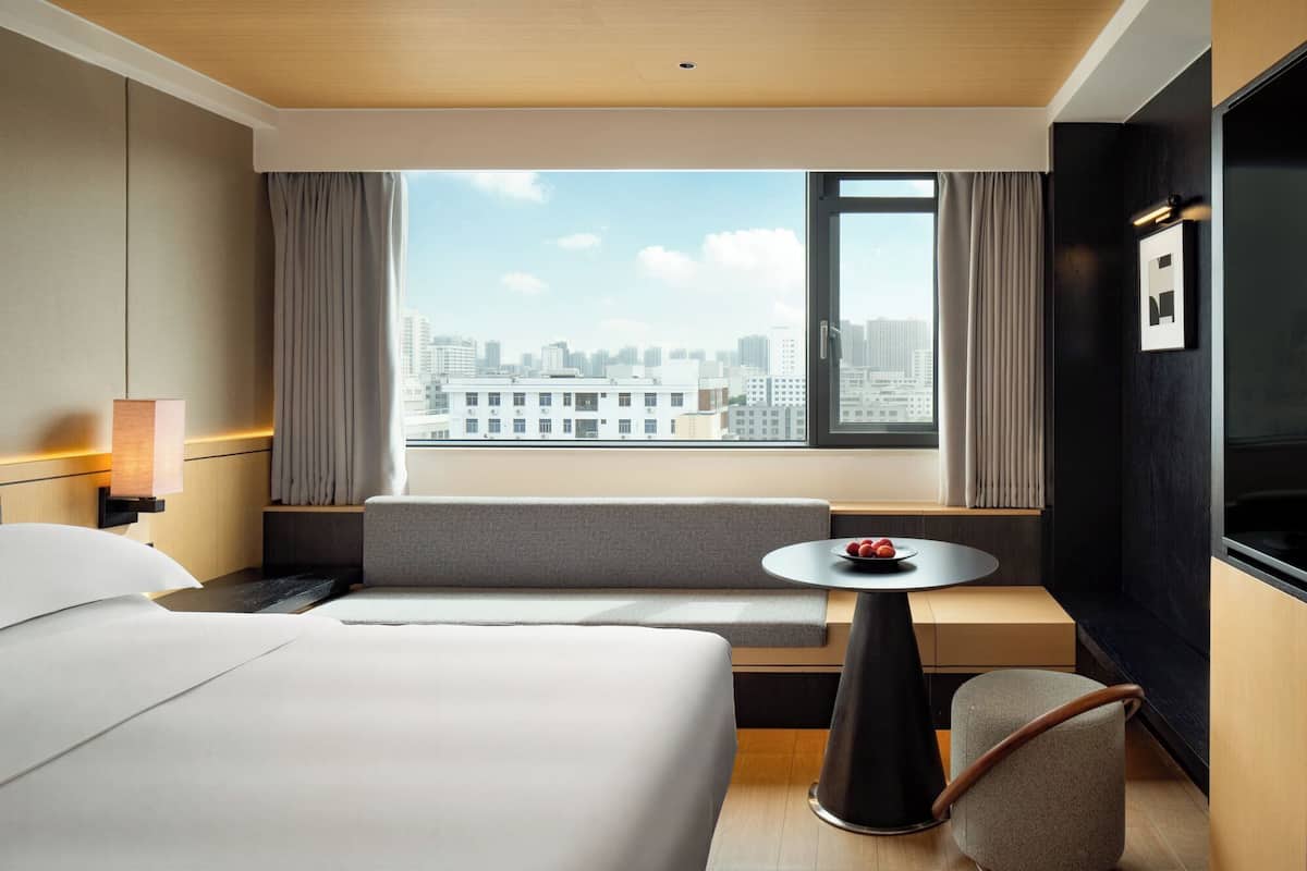 Une chambre d’hôtel avec un lit, un coin salon, une petite table avec des fruits, une télévision et une vue sur la ville.
