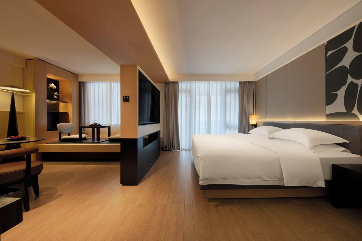 Une chambre d’hôtel avec un lit, un bureau et une chaise, une télévision et une grande fenêtre avec des rideaux.