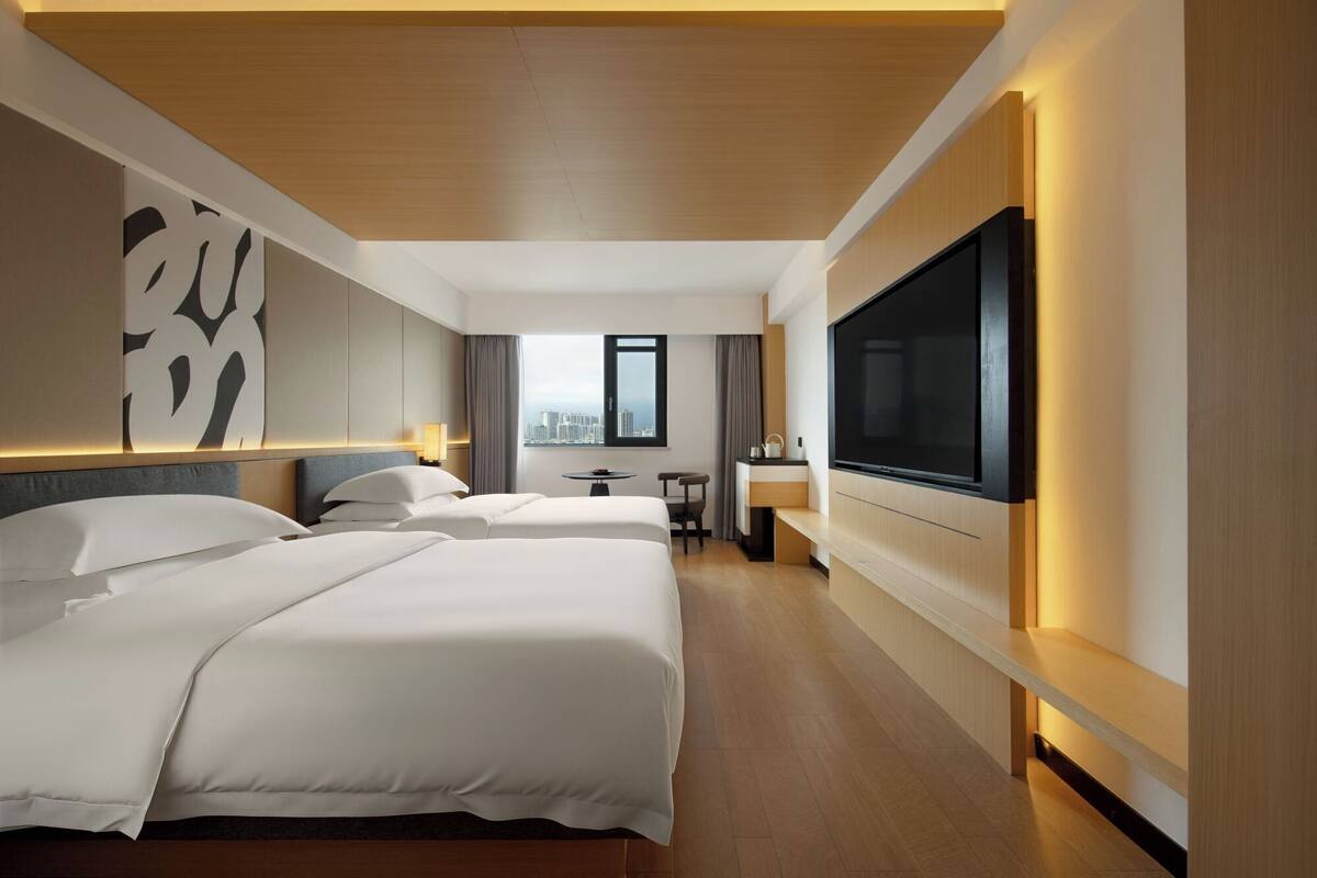Une chambre d’hôtel avec deux lits, une télévision, un bureau et une vue sur la ville.
