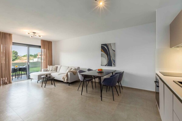 A modern living room with a sofa, dining table, chairs, and a kitchen area. - Holiday apartment modernly furnished with full equipment (Funtana)