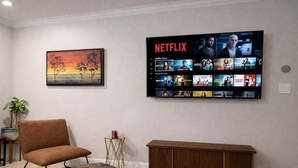 Ein Wohnzimmer mit einem großen Flachbildfernseher, der Inhalte von Netflix zeigt, einem braunen Ledersessel, einem Holznachttisch und einem Gemälde an der Wand.