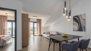Una sala de estar moderna con sofá, mesa de comedor y sillas, un ventanal con cortinas y una lámpara de techo.
