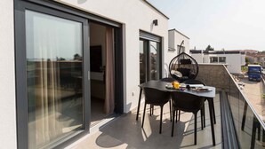 Un balcón moderno con puerta de vidrio, una mesa con sillas y una silla colgante.
