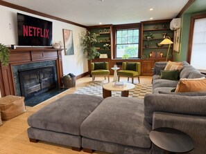 A living room with a fireplace, a television, and a bookshelf. - Lux Colonial Home: Hot tub, Game Room, Home Theatre, Karaoke (Framingham)