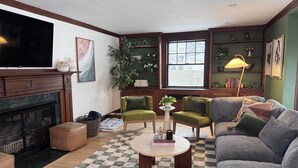 Una sala de estar con chimenea, sillones verdes, un sofá, una mesa de centro y un televisor.