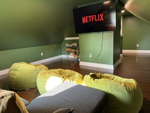 A room with green walls, a flat-screen TV mounted on the wall displaying 'NETFLIX', and a wooden floor. - Lux Colonial Home: Hot tub, Game Room, Home Theatre, Karaoke (Framingham)