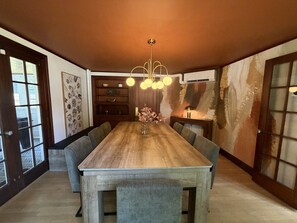 A dining area with a long wooden table, upholstered chairs, and a modern chandelier. - Lux Colonial Home: Hot tub, Game Room, Home Theatre, Karaoke (Framingham)