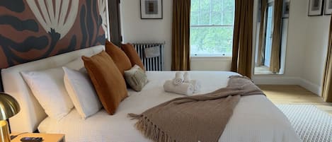 A neatly made bed with a white comforter and a brown throw blanket, a bedside lamp, and a framed picture on the wall.