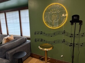 A room with a green wall featuring a neon sign for Boston's Karaoke Bar, a stool, and a microphone stand. - Lux Colonial Home: Hot tub, Game Room, Home Theatre, Karaoke (Framingham)