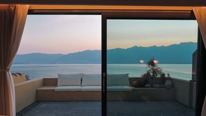 Un balcon avec un canapé et des coussins, un petit arbre, et une vue sur une étendue d’eau et des montagnes.