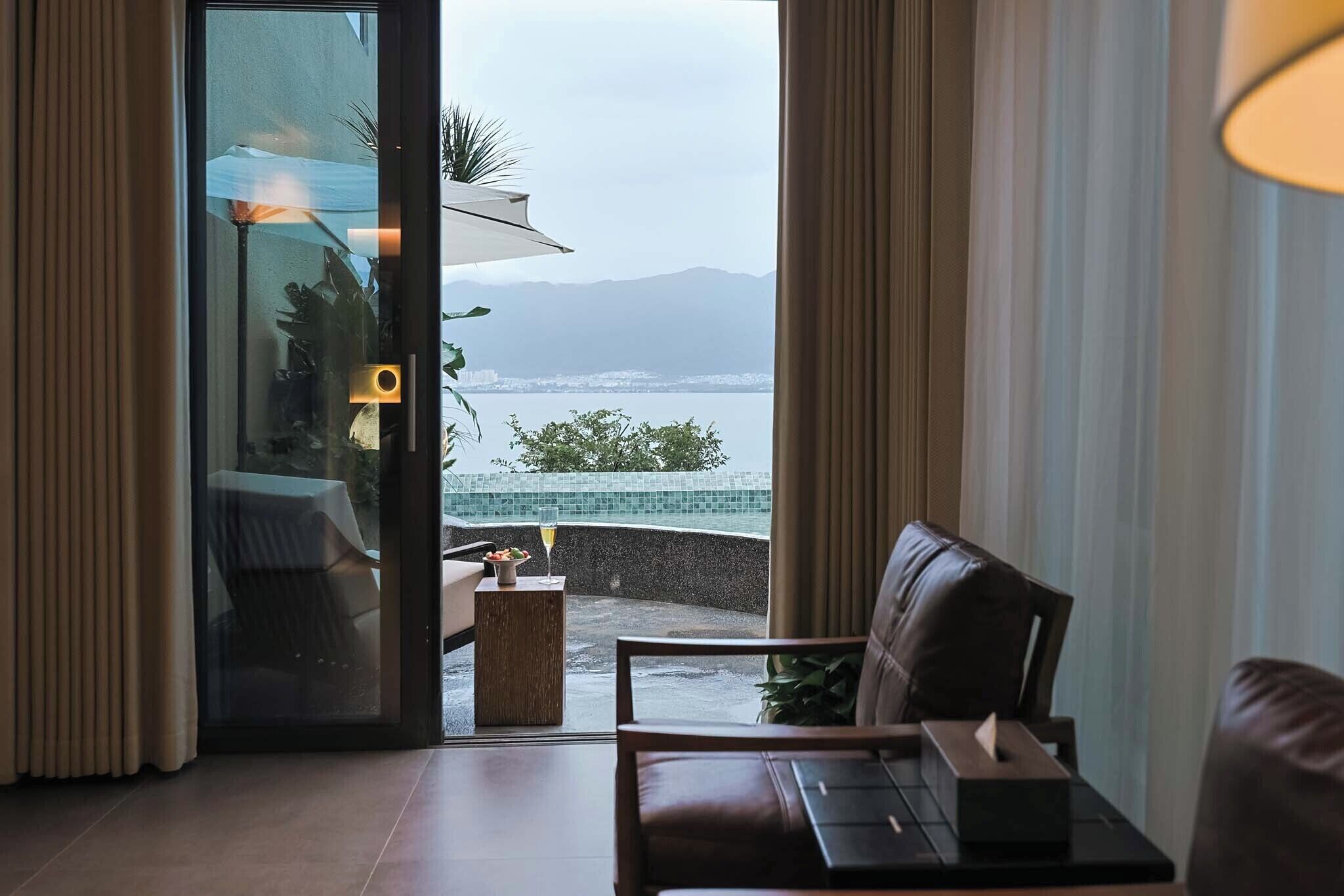 Ein Zimmer mit Glastür und Zugang zu einem Balkon mit Blick auf das Meer und die Berge.