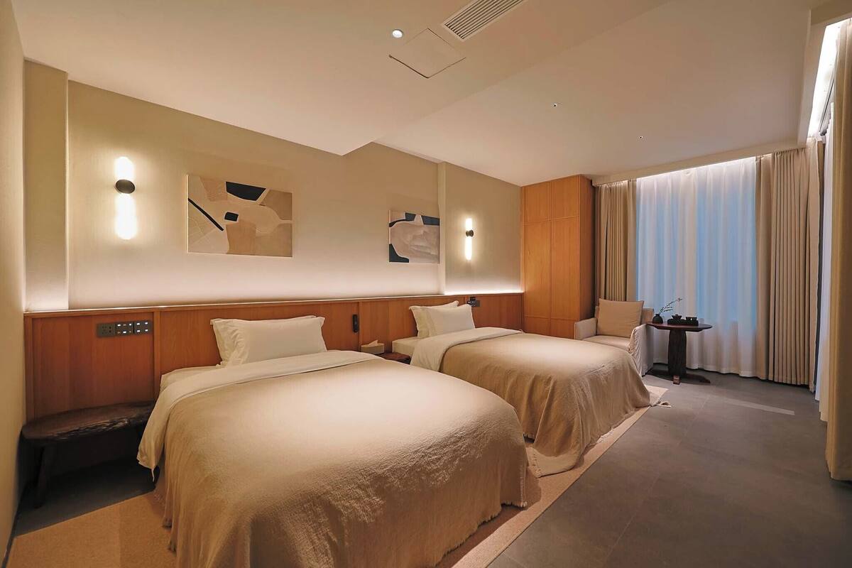 A hotel room with two beds, a small table, a chair, and artwork on the walls.