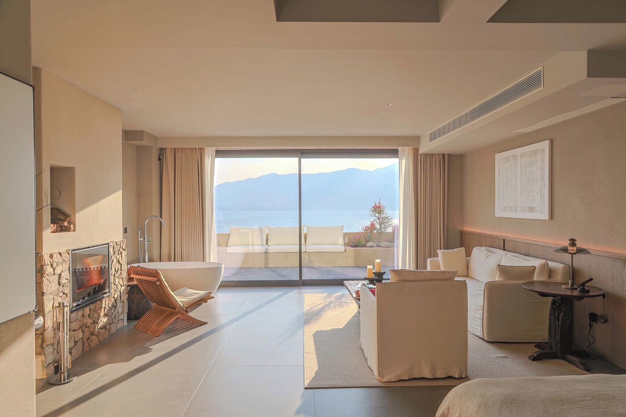 A modern hotel room with a fireplace, a sofa, a dining table, and a view of the mountains.