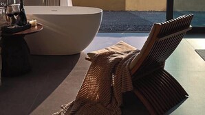 Une salle de bain moderne avec une baignoire sur pieds, une douche à parois de verre et une grande fenêtre offrant une vue sur la mer et les montagnes.