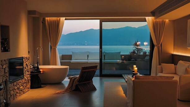 Une chambre moderne dotée d’une grande baignoire, d’un canapé, d’une télévision et offrant une vue sur la mer et les montagnes.