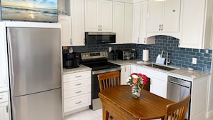 A modern kitchen with white cabinets, stainless steel appliances, a flat-screen TV, and a dining area with a wooden table and chairs. - Venice Villas San Marco - Oceanfront - Beach (Venice)
