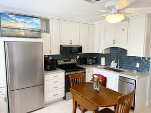A modern kitchen with white cabinets, stainless steel appliances, a flat-screen TV, and a dining area with a wooden table and chairs. - Venice Villas Luxury Beachfront – Steps to Sand (Venice)