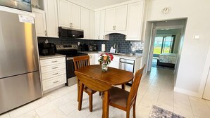 A modern kitchen with white cabinets, stainless steel appliances, and a dining area with a wooden table and chairs. - Venice Villas San Marco - Oceanfront - Beach (Venice)