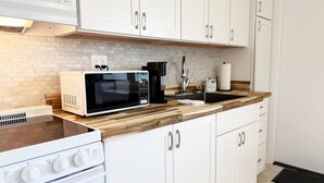Une cuisine avec des meubles blancs, un four à micro-ondes, une machine à café et une cuisinière.