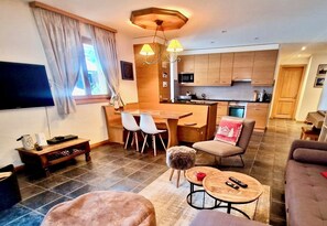 Un salon moderne doté d’un téléviseur à écran plat, d’un coin repas avec des chaises, d’une cuisine avec des meubles en bois et d’un canapé.