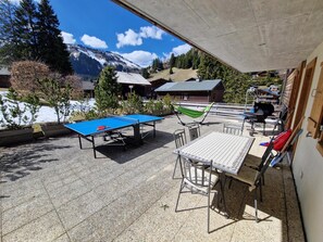 Une table de ping-pong, des chaises et une table offrant une vue sur les montagnes et les bâtiments.