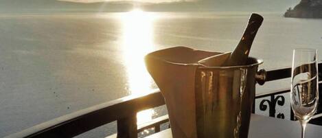 A table with a bottle of champagne, a glass, and a view of the sea at sunset.