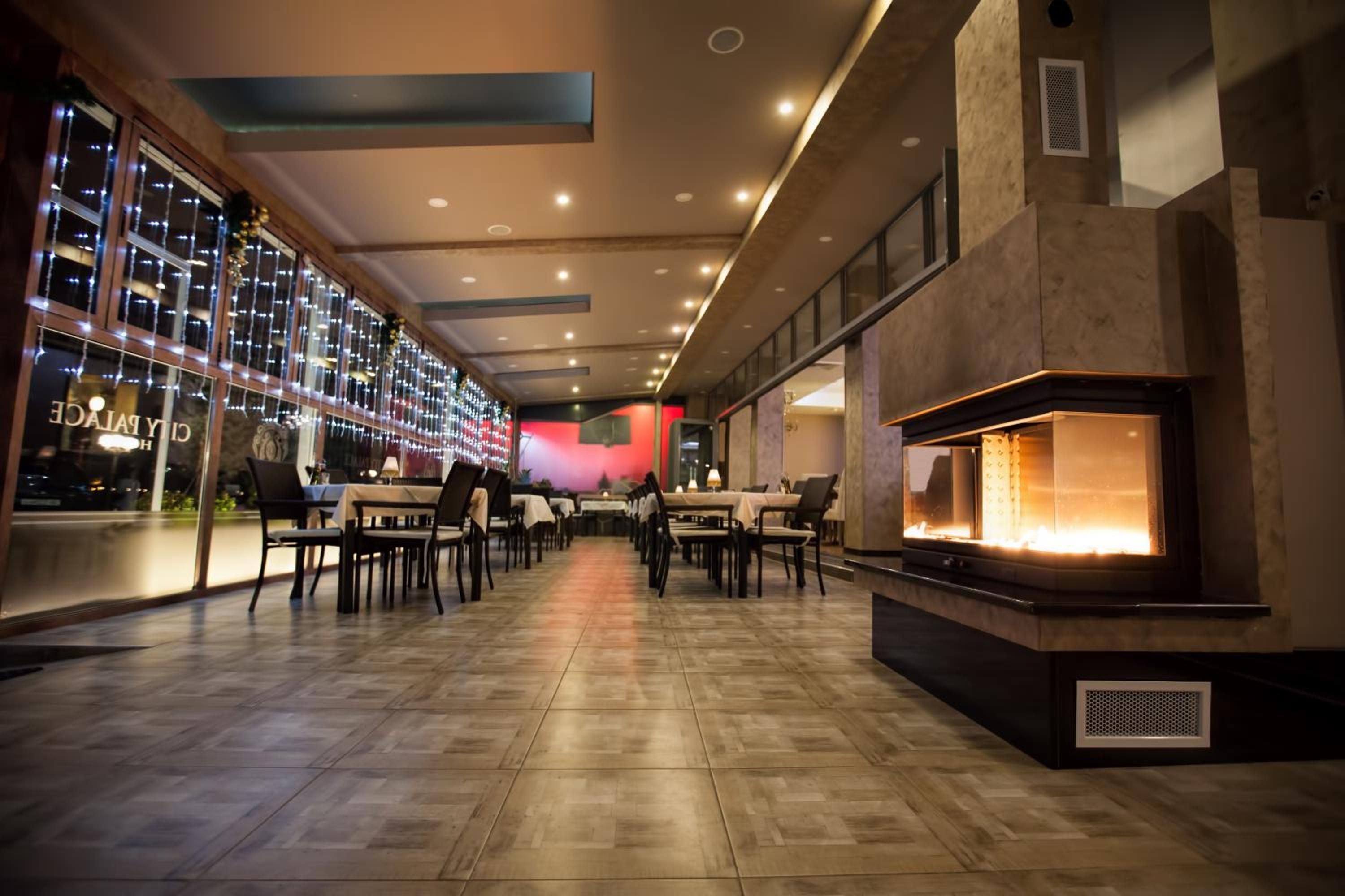 A spacious indoor area with a long row of tables and chairs, a fireplace, and a wall with a patterned design.