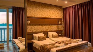 Camera d'albergo con un letto grande, una testiera in legno, un comodino e vista sul mare.