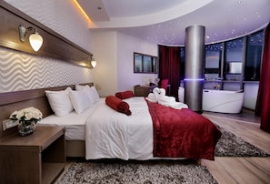 Una habitación de hotel moderna con una cama grande, zona de estar, vistas de la ciudad y baño con bañera.