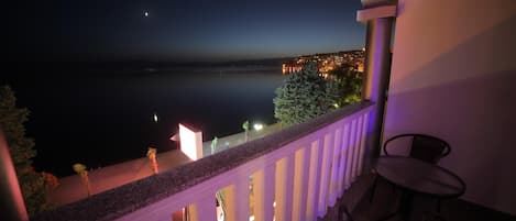 A balcony with a view of a calm body of water and a lit-up town in the distance.